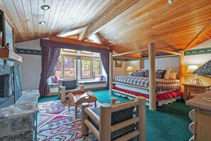 A cozy room with a fireplace, a bed with a plaid bedspread, a window with curtains, and a wooden ceiling. - La Maconnerie Cabin - Ski In-Ski Out (Park City)