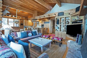 L’intérieur d’une cabane en rondins, avec un salon chaleureux, des meubles en bois, une cheminée et une cuisine.