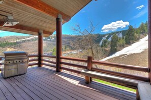 Une terrasse en bois avec un barbecue et un banc, offrant une vue sur un paysage montagneux.