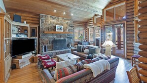 A log cabin interior with a stone fireplace, wooden furniture, and a large flat-screen TV. - La Maconnerie Cabin - Ski In-Ski Out (Park City)