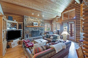 L’intérieur d’une cabane en rondins, avec une cheminée en pierre, des meubles en bois et un grand téléviseur à écran plat.