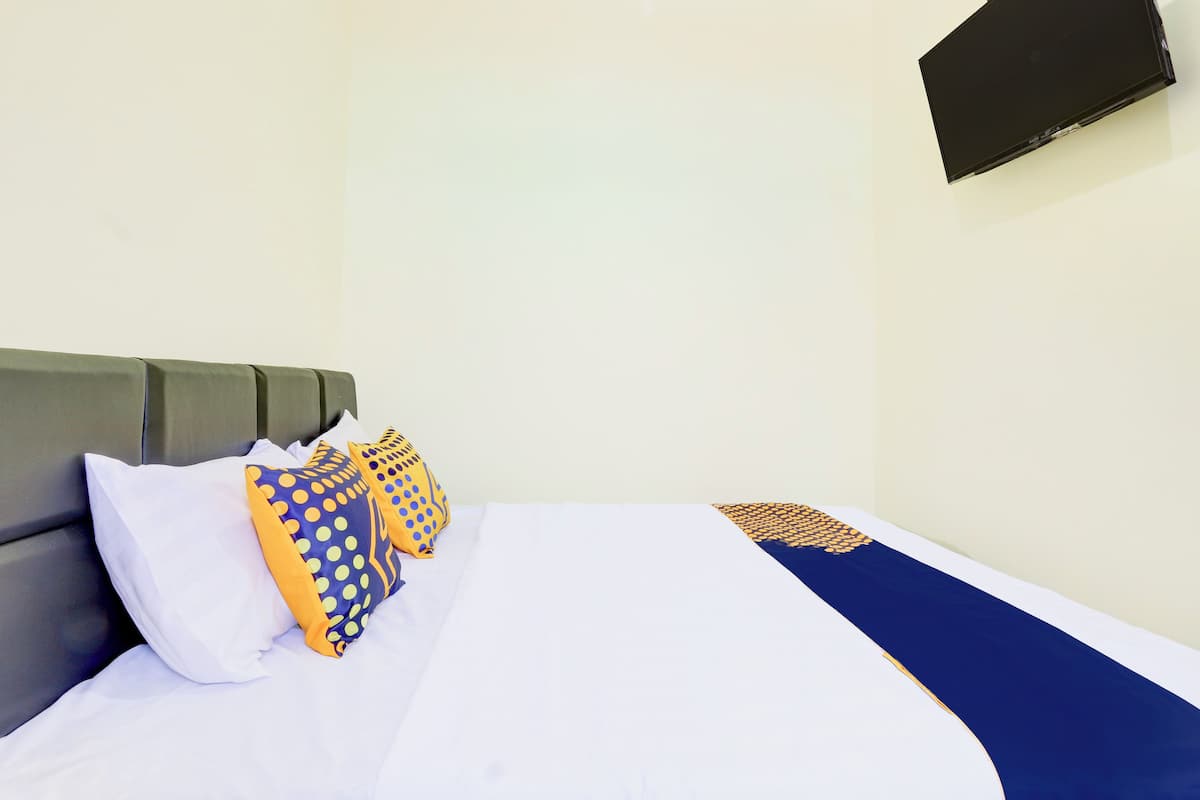 A hotel room with a bed, pillows, a flat-screen TV, and a wall-mounted TV.