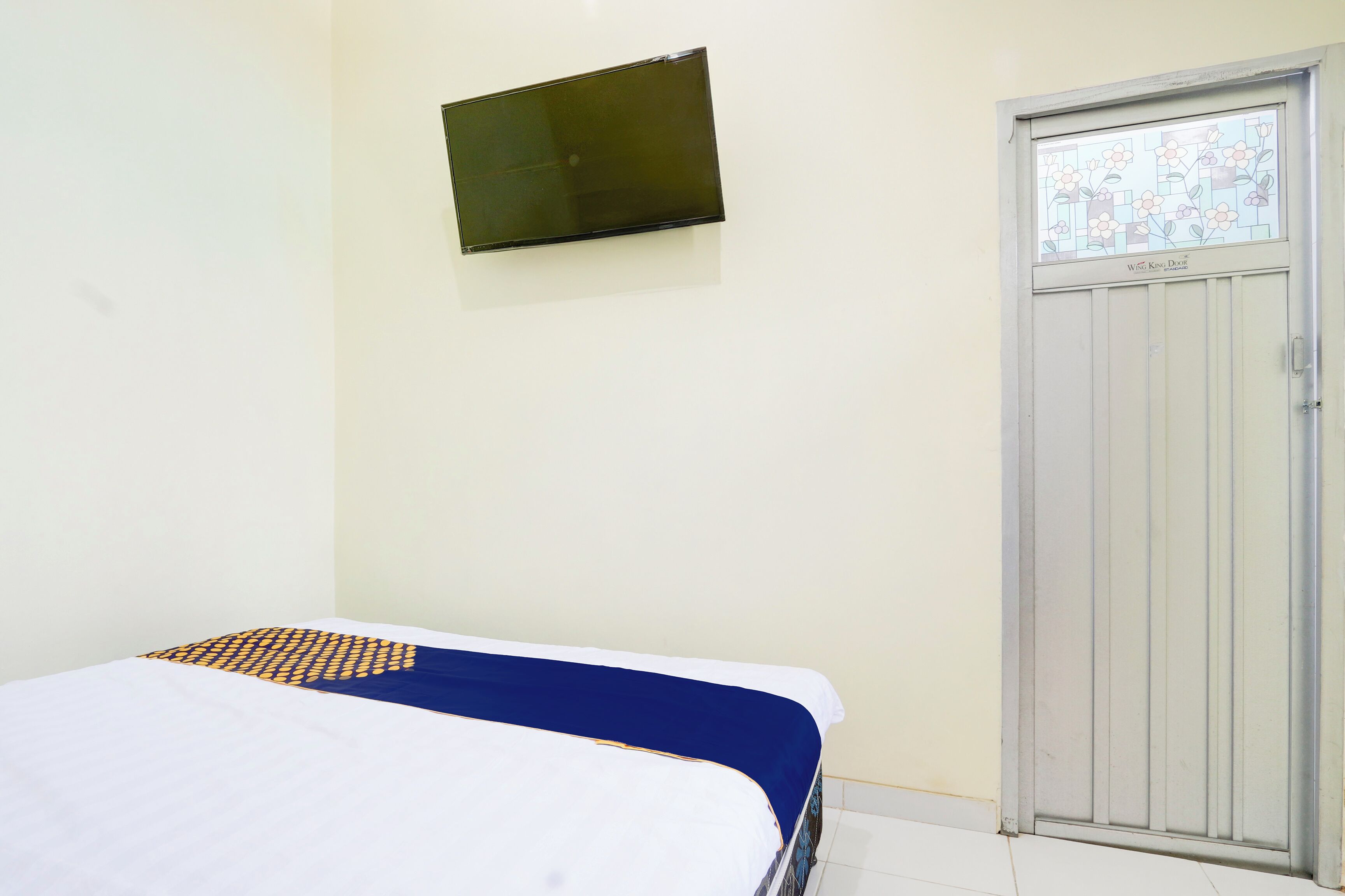 A room with a bed, a television mounted on the wall, and a door with a window.