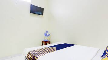 Un dormitorio con cama, televisor montado en la pared y ventilador de pie.