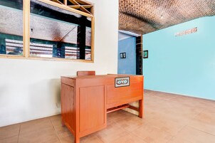 Quarto com escrivaninha de madeira, janela com vista para um edifício, teto trabalhado e parede azul.
