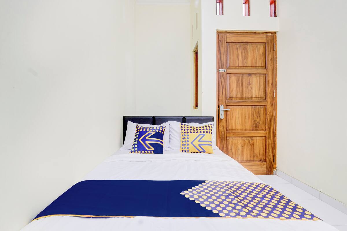 A bed with white bedding and a blue and yellow patterned throw.
