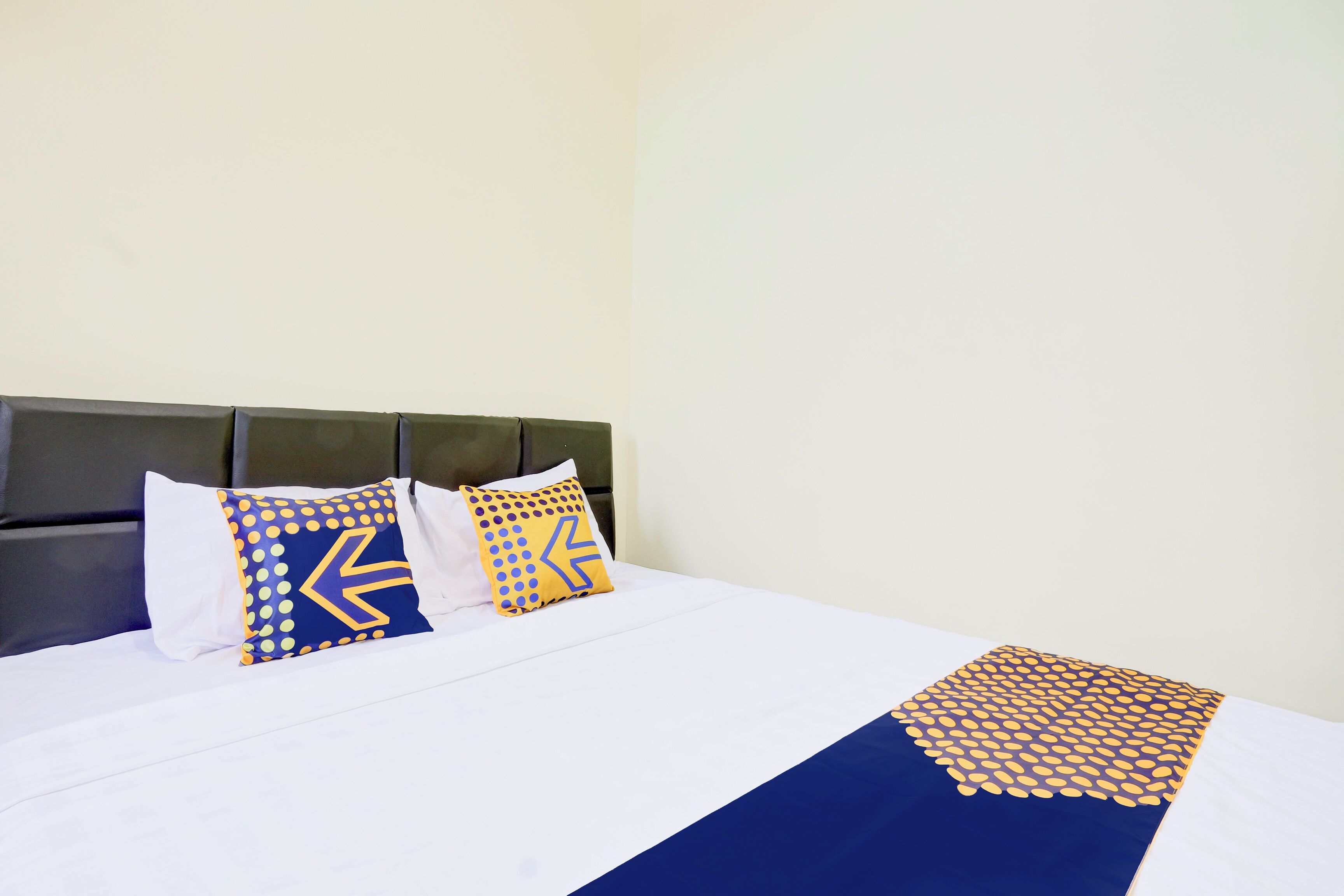 Een net opgemaakt bed met een blauw-witte dekbedovertrek en twee decoratieve kussens met geometrische patronen.
