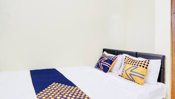 Una cama con una colcha blanca y azul, dos almohadas con diseños geométricos y un cabecero de madera.