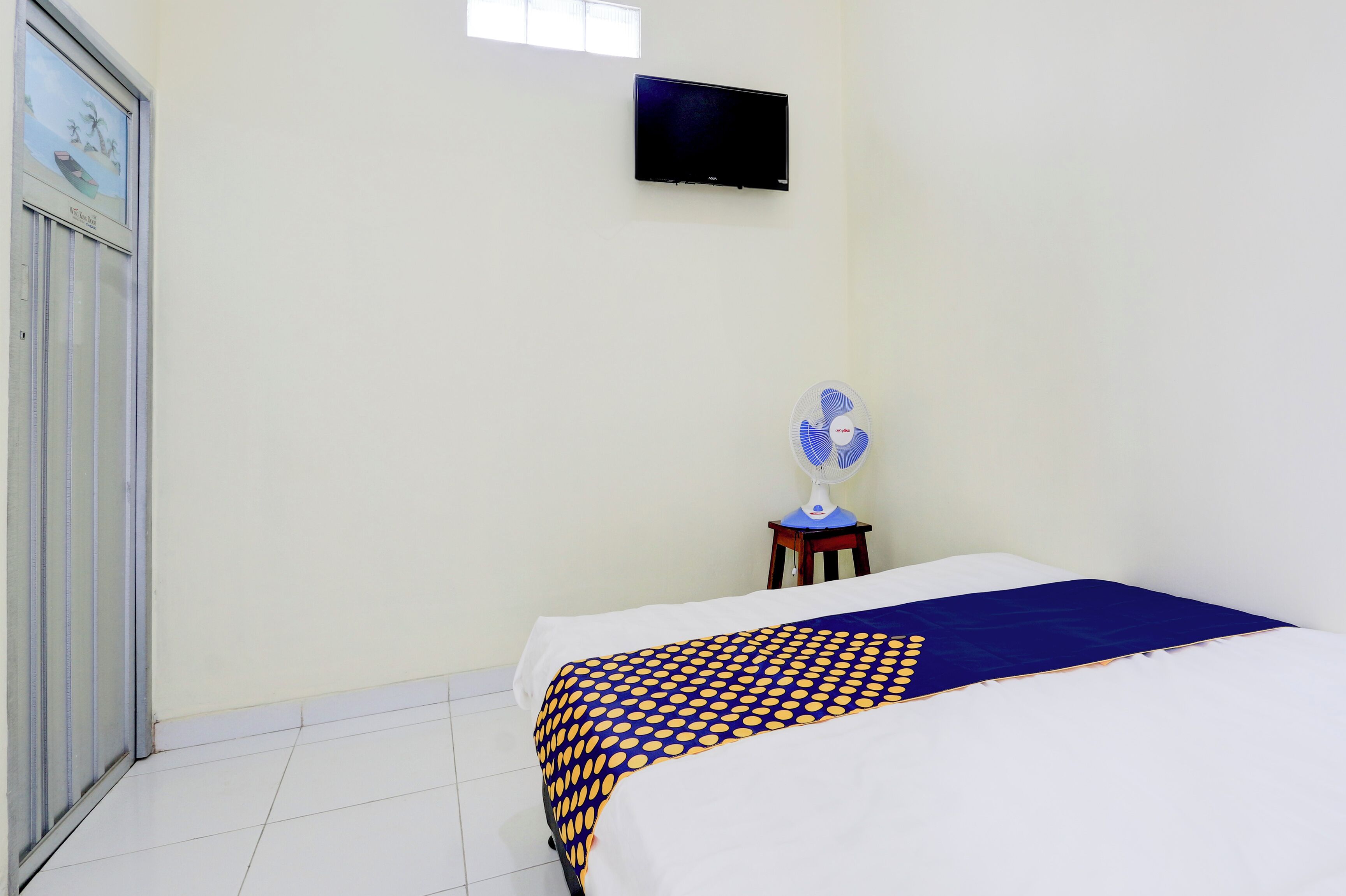 A bedroom with a bed, a TV mounted on the wall, and a fan on a small table.
