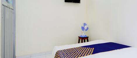 A bedroom with a bed, a TV mounted on the wall, and a fan on a small table.