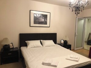 A neatly made bed with white linens, a framed picture on the wall, a chandelier, and a door in the background. - LILU HOUSE ,5-bedroom villa in peaceful Câmpina with WiFi (Câmpina)