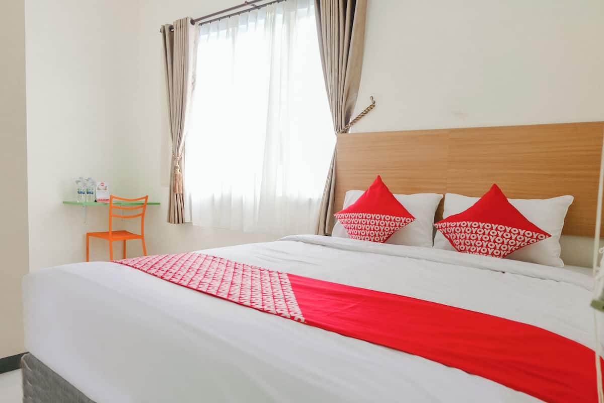 Una cama bien hecha con ropa de cama roja y blanca, un cabecero de madera y dos almohadas rojas con diseños blancos.