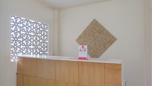 Una zona de recepción con mostrador de madera, ventana con diseño y un adorno de pared en forma de diamante.