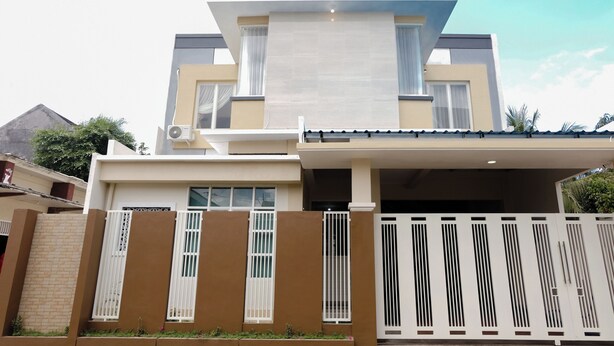 Una casa moderna de dos plantas con techo plano, ventanas amplias y entrada protegida por un portón.