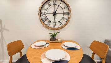 Una mesa redonda con cuatro platos y dos sillas, un reloj de pared grande y una planta pequeña sobre la mesa.