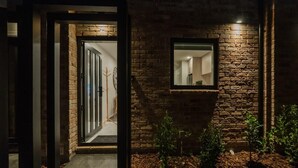 Fachada de ladrillo con una puerta que da a un espacio interior, una ventana pequeña y una planta en primer plano.