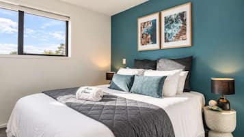 Un dormitorio con cama, almohadas, una lámpara de noche y dos cuadros en la pared.