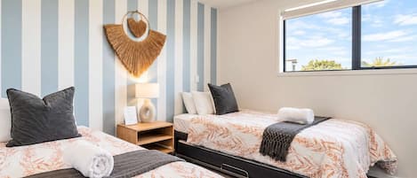 Habitación de hotel con dos camas, una mesita de noche, una lámpara de pared y ventana con vistas.