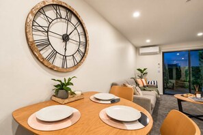 Un coin repas avec une grande horloge murale, une table dressée avec des assiettes et un canapé en arrière-plan.