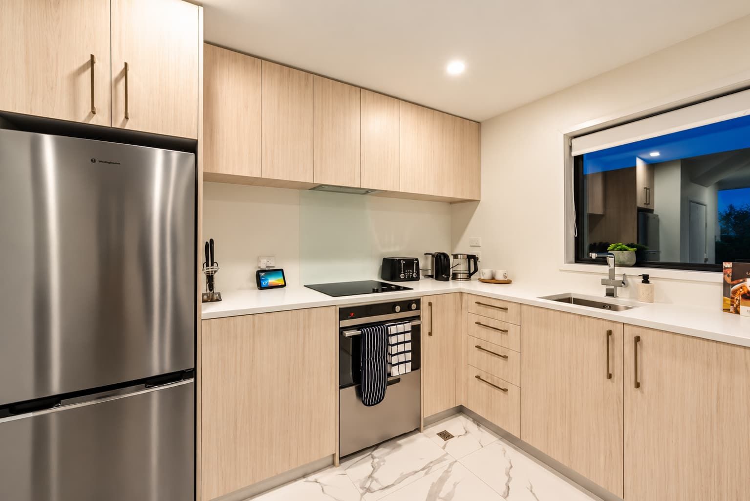 A modern kitchen with stainless steel appliances, wooden cabinets, and a marble floor.