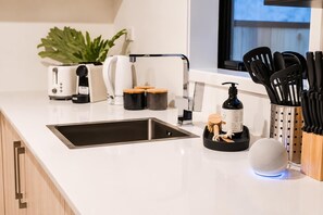 A modern kitchen with a stainless steel sink, a coffee maker, a plant, and a set of knives. - Central 2BR Townhouse | Near CBD + Stadium (Christchurch)
