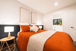 Une chambre d’hôtel avec un lit, une table de chevet avec une lampe, un téléviseur fixé au mur et une porte avec un miroir.