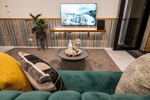 Ett modernt vardagsrum med en platt-TV som är monterad på en vägg av trä, ett runt soffbord med dekorativa föremål och en grön soffa med en gul kudde.