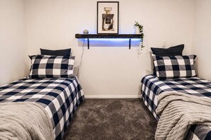 A room with two beds, each with a checkered bedspread and matching pillows. There is a shelf with a framed picture above the beds.