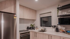 A modern kitchen with stainless steel appliances, light wood cabinets, and a built-in microwave.
