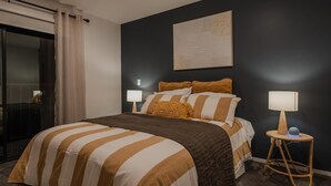 A bedroom with a bed, two bedside tables, a wall-mounted artwork, and a sliding door.