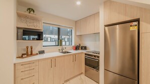 Una cocina moderna con armarios de madera clara, un refrigerador de acero inoxidable y un ventanal que proporciona luz natural.
