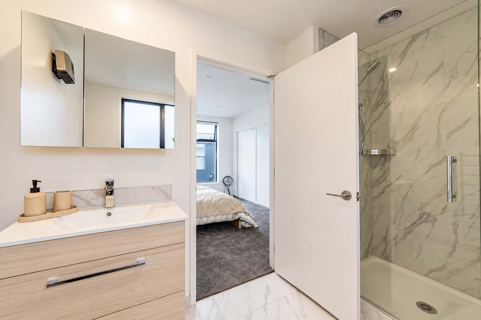 A modern bathroom with a marble shower, a large mirror, and a vanity with a sink and storage.