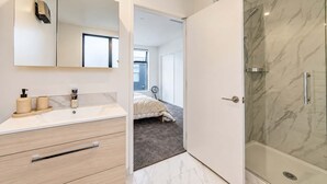 Une salle de bain moderne avec une douche en marbre, un grand miroir et un meuble-lavabo avec un évier et des rangements.