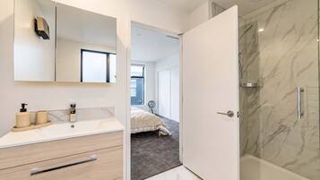 A modern bathroom with a marble shower, a large mirror, and a vanity with a sink and storage.