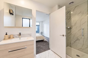 A modern bathroom with a marble shower, a large mirror, and a vanity with a sink and storage. - CBD 2BR Retreat | Private Garden + BBQ (Christchurch)