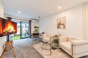 A modern living room with a flat-screen TV, a sofa, a coffee table, and a fireplace. - CBD 2BR Retreat | Private Garden + BBQ (Christchurch)
