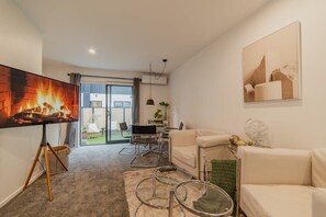 A modern living room with a flat-screen TV, a sofa, a coffee table, and a dining area with chairs and a table.