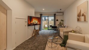 Una sala de estar moderna con un televisor de pantalla plana, un sofá, una mesa de centro y un comedor con sillas.