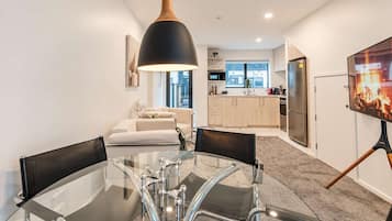A modern kitchen with a large window, a dining area with a glass table, and a living room with a sofa.
