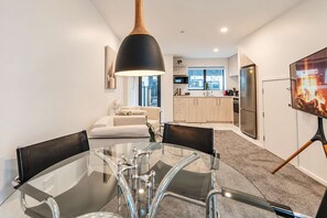 A modern kitchen with a large window, a dining area with a glass table, and a living room with a sofa. - CBD 2BR Retreat | Private Garden + BBQ (Christchurch)