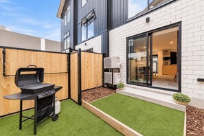 Ett modernt hus med en trädgård, en grill och en glasdörr som leder in till ett inomhusutrymme.
