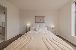 Una camera da letto con un letto grande, due comodini con lampade, un quadro appeso al muro e un tappeto a motivi ondulati.