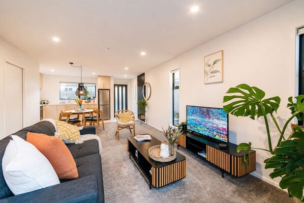 A modern living room with a sofa, coffee table, TV, and dining area.