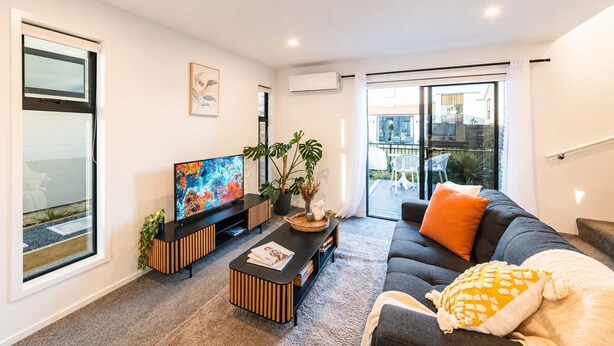 Uma sala de estar moderna com televisão de tela plana, sofá, mesinha de centro e um vaso de planta.