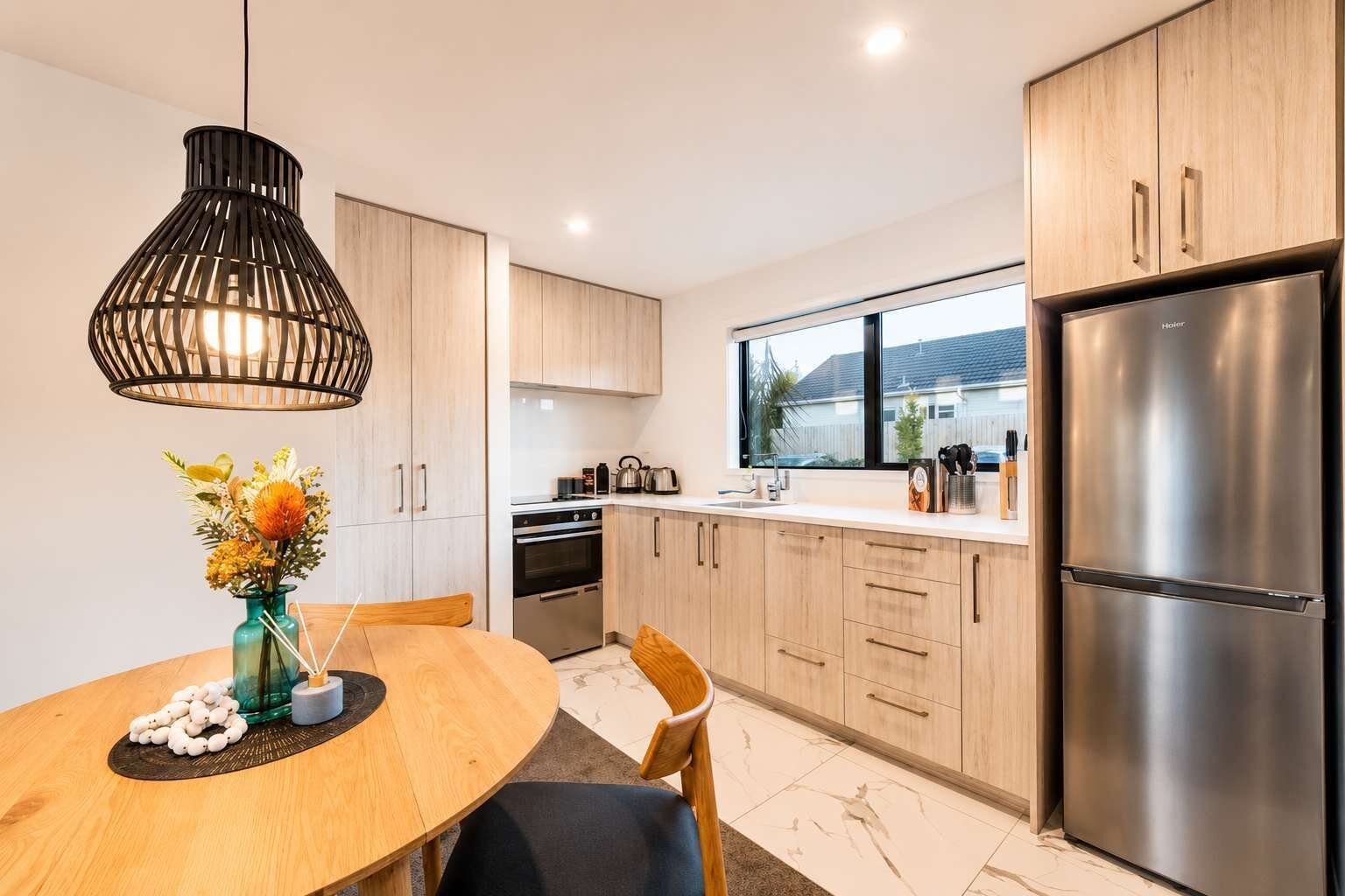 A modern kitchen with wooden cabinets, a stainless steel refrigerator, and a dining area with a table and chairs.