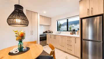 A modern kitchen with wooden cabinets, a stainless steel refrigerator, and a dining area with a table and chairs.