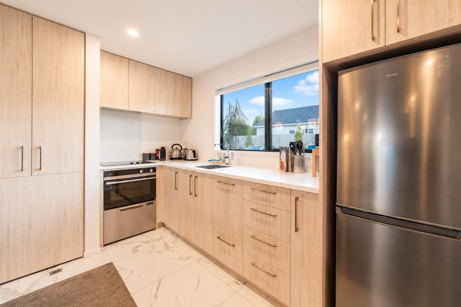 Una cocina moderna con armarios de madera clara, electrodomésticos de acero inoxidable y un ventanal con vistas al exterior.