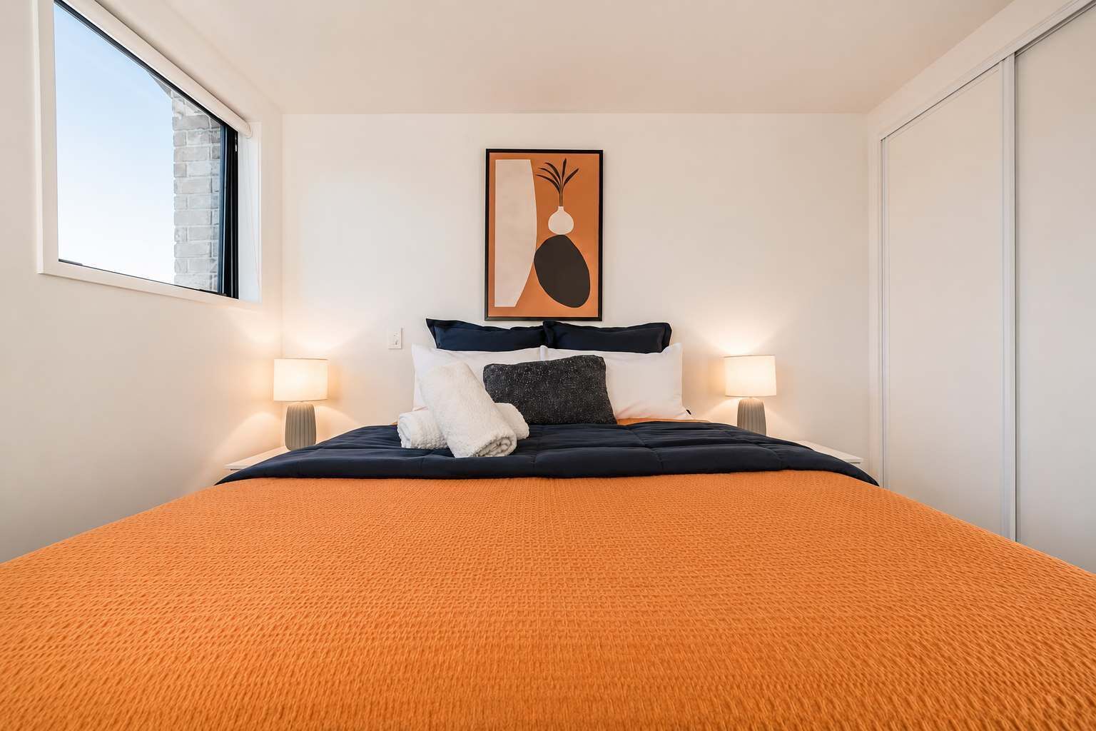 Habitación de hotel con cama, dos lámparas de noche, un cuadro enmarcado sobre la cama y una ventana a un lado.