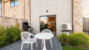 Un patio moderno al aire libre con una parrilla, dos sillas blancas y una mesa.