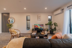 A modern living room with a sofa, a television, a coffee table, and two potted plants.